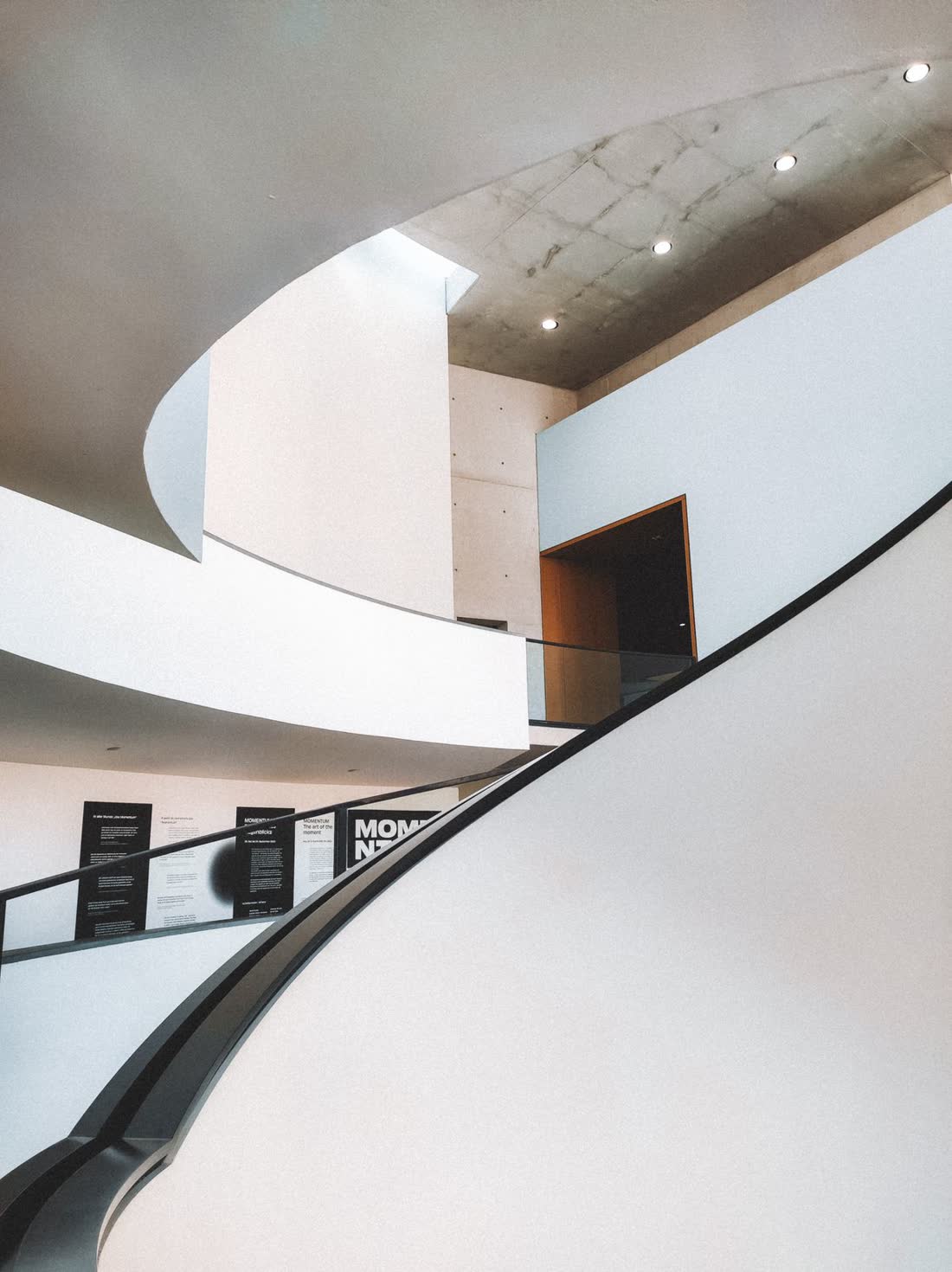 A pale curved staircase rising through daylight