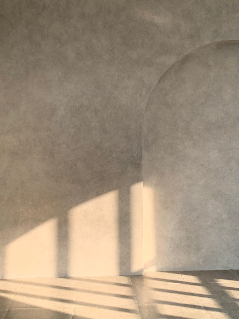 Afternoon light crossing a plastered wall beside an arch, moved on by the hour